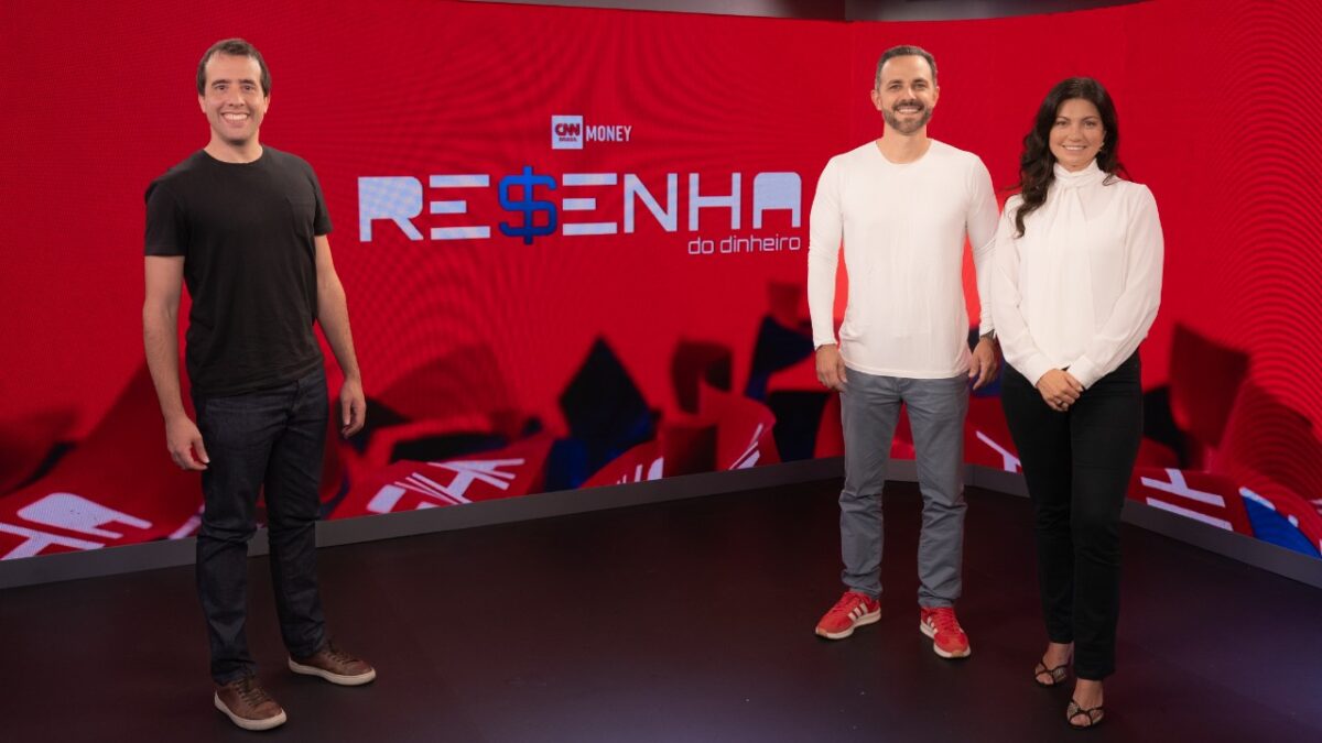 Bernardo Pascowitch, Thiago Godoy e Marília Fontes posam no cenário do programa Resenha do Dinheiro, da CNN Money, diante de um telão vermelho vibrante