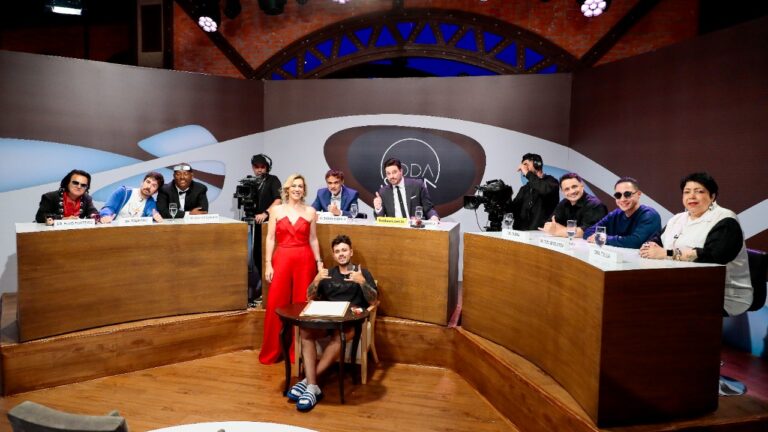 Camila Gentile de macacão vermelho no centro do cenário do quadro Roda Solta, programa The Noite com Danilo Gentili, cercada por convidados e bancadas