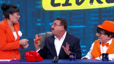 Carlos Massa, o Ratinho, de terno azul e camisa branca, gesticula entre Milene Pavorô de blazer laranja e Santos de colete e chapéu laranjas no SBT