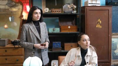 Hazar Erguclu como Cicek veste blazer xadrez e segura xícara de chá, enquanto Dilan Cicek Deniz como Ruya usa casaco bege em cena de Chamas do Destino