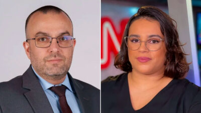 Daniel Rittner, de terno cinza, e Jenifer Ribeiro, de blusa branca, sorriem no cenário da CNN Brasil, fundo com monitores e iluminação azulada