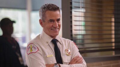 Dom Pascal interpretado por Dermot Mulroney sorri de braços cruzados usando uniforme de bombeiro em cena da série Chicago Fire