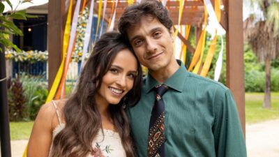 Larissa Manoela como Estela e Cadu Libonati como Túlio posam com cabeças encostadas, ela sorri com vestido floral, ele veste camisa verde e gravata estampada