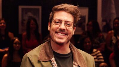 Fábio Porchat sorrindo com óculos em gravação do programa Que História É Essa Porchat? com plateia ao fundo