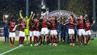 Jogadores do Flamengo comemoram o bicampeonato da Libertadores Sub-20 no gramado, sob chuva de confetes dourados, enquanto um atleta ergue a taça