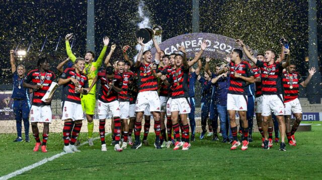 Jogadores do Flamengo comemoram o bicampeonato da Libertadores Sub-20 no gramado, sob chuva de confetes dourados, enquanto um atleta ergue a taça