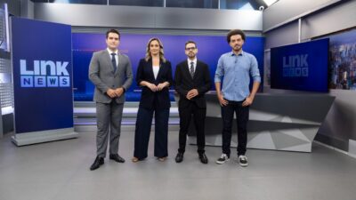 Gustavo Toledo, Daysa Belini, Renato Diniz e Caique Rezende posam no estúdio do Link News com telões e bancada ao fundo