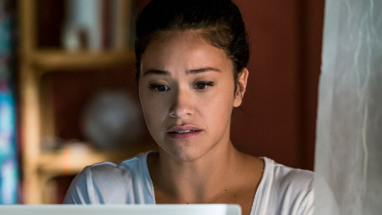 Gina Rodriguez como Jane Villanueva aparece com expressão de preocupação e apreensão enquanto olha para a tela de um computador na série Jane, a Virgem