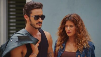 Filipe Bragança como João Raul de óculos escuros e Isadora Cruz como Agrado de jaqueta jeans conversam seriamente em cena da novela Coração Acelerado