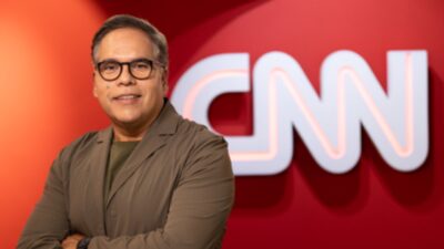 Jorge Moraes de braços cruzados diante de painel vermelho com logotipo da CNN ao fundo