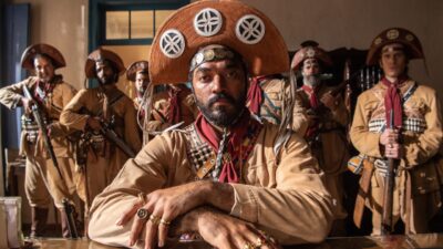 Thomás Aquino como Josué sentado à frente de grupo de cangaceiros armados em cena da novela Guerreiros do Sol