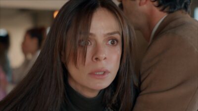 Ozge Ozpirincci interpreta Karsu na novela Coração de Mãe com expressão de espanto, olhos arregalados, cabelos castanhos lisos e gola alta escura