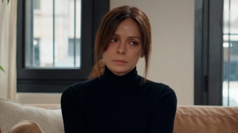 Ozge Ozpirincci, como a protagonista Karsu na novela Coração de Mãe, encara o nada com olhar triste e pensativo, vestindo uma blusa preta de gola alta