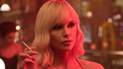 Lorraine Broughton (Charlize Theron) segura cigarro em bar iluminado por luz vermelha no filme Atômica