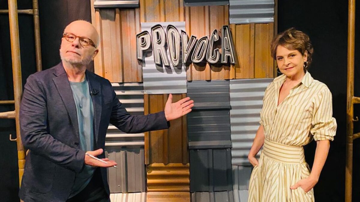 Marcelo Tas gesticula em frente ao letreiro Provoca enquanto Drica Moraes posa ao lado no cenário do programa da TV Cultura