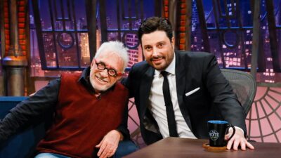 Moacyr Franco usa colete bordô e Danilo Gentili veste terno preto, ambos sorriem abraçados no cenário do programa The Noite