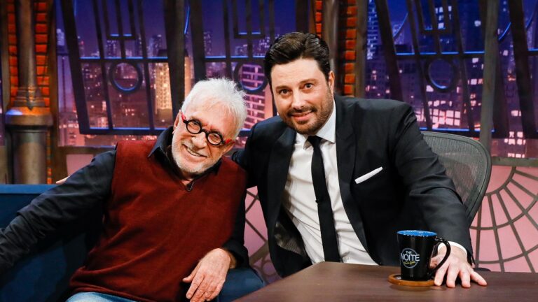 Moacyr Franco usa colete bordô e Danilo Gentili veste terno preto, ambos sorriem abraçados no cenário do programa The Noite