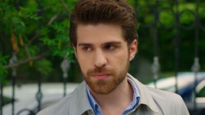 Berker Guven interpreta Nedim na novela Cruel Istambul, ator possui barba ruiva aparada e topete castanho, veste camisa listrada e casaco bege claro