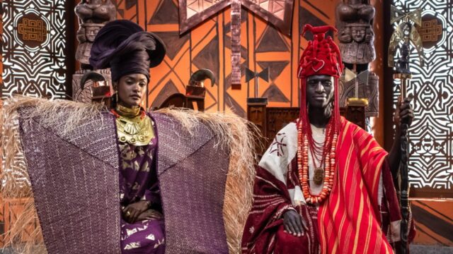 Erika Januza como Rainha Niara e Welket Bungué como Rei Cayman II posam em tronos, usando trajes africanos de gala, coroas e colares em tons de roxo e vermelho