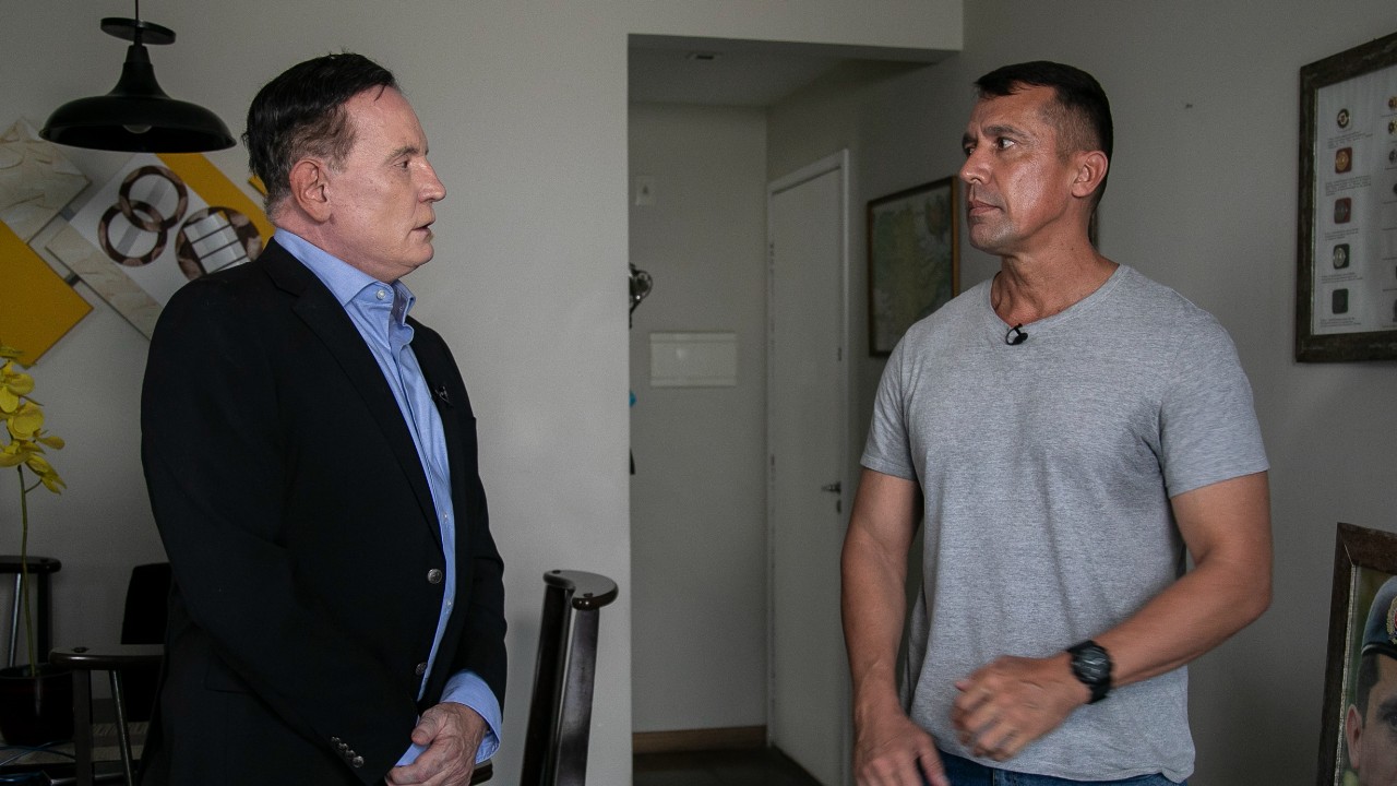 Roberto Cabrini entrevista o tenente-coronel Geraldo Rosa Neto em sala com quadros na parede durante reportagem