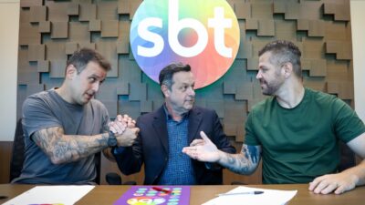 Rodrigo Capella, Mauro Lissoni e Victor Sarro apertam as mãos em reunião com logo do SBT ao fundo