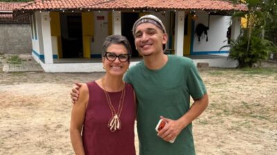 Sandra Annenberg e João Gomes abraçados e sorrindo em frente a casa rural durante gravação do Globo Repórter