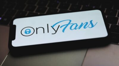 Logo do OnlyFans exibido na tela de smartphone sobre teclado de laptop em referência a conteúdos de celebridades