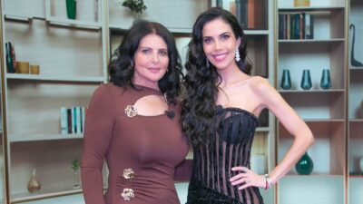Sônia Lima de vestido marrom e Daniela Albuquerque com traje preto transparente sorriem abraçadas no cenário do programa Sensacional da RedeTV!