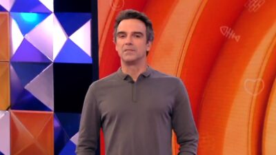 Tadeu Schmidt apresenta o BBB 26 usando camisa polo cinza de mangas longas, apresentador aparece à frente de cenário com painéis geométricos coloridos