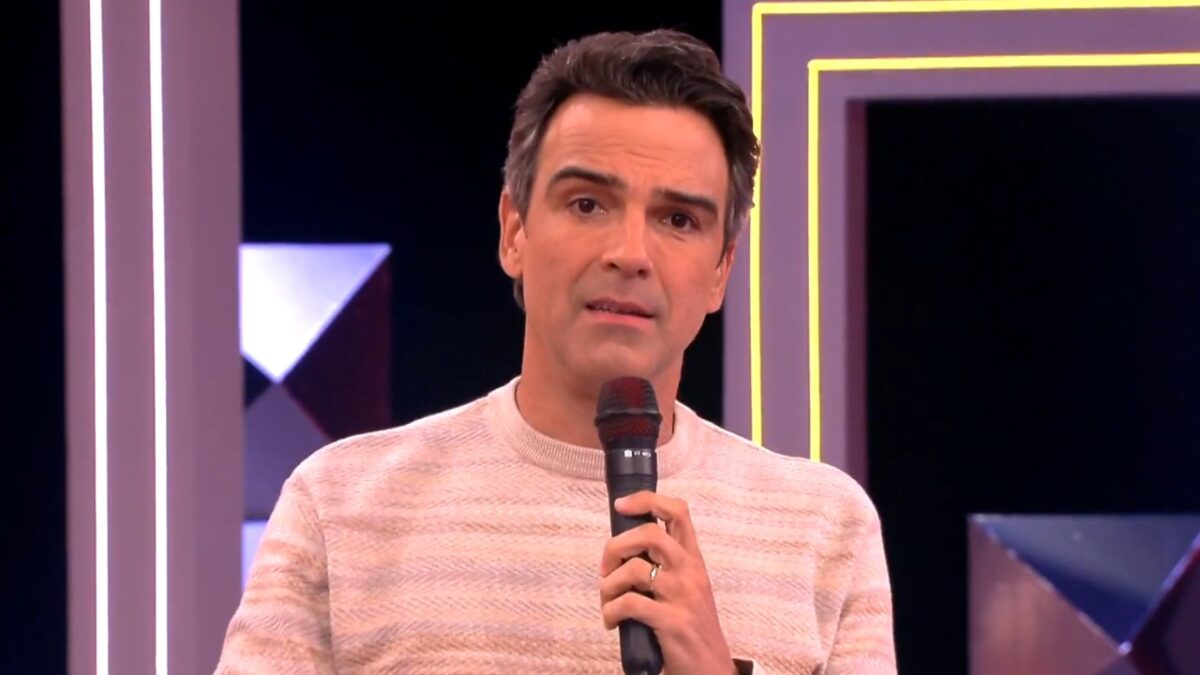 Tadeu Schmidt segura microfone e fala ao público no palco do BBB 26 com cenário iluminado ao fundo