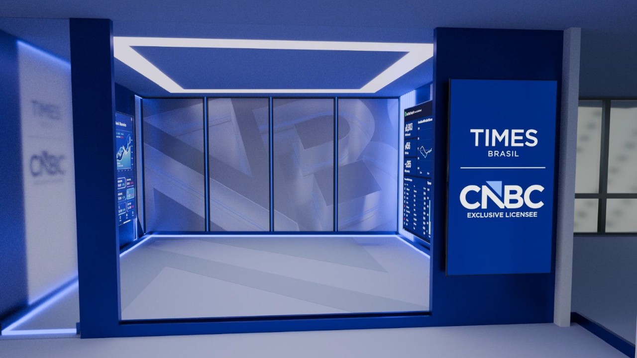 Vista do estúdio Times Brasil | CNBC com janelas amplas mostrando cidade e tela com gráficos de mercado e dados financeiros em painel digital