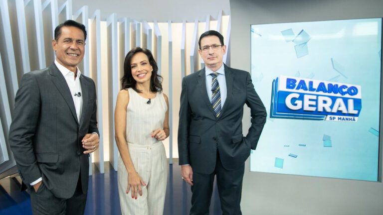 Willian Leite de terno cinza, Fabiana Oliveira de conjunto bege e Roberto Guastelli de terno escuro sorriem ao lado do telão do Balanço Geral Manhã