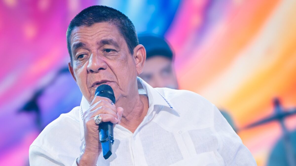 Zeca Pagodinho canta ao microfone no palco do Altas Horas com luzes coloridas e músicos ao fundo