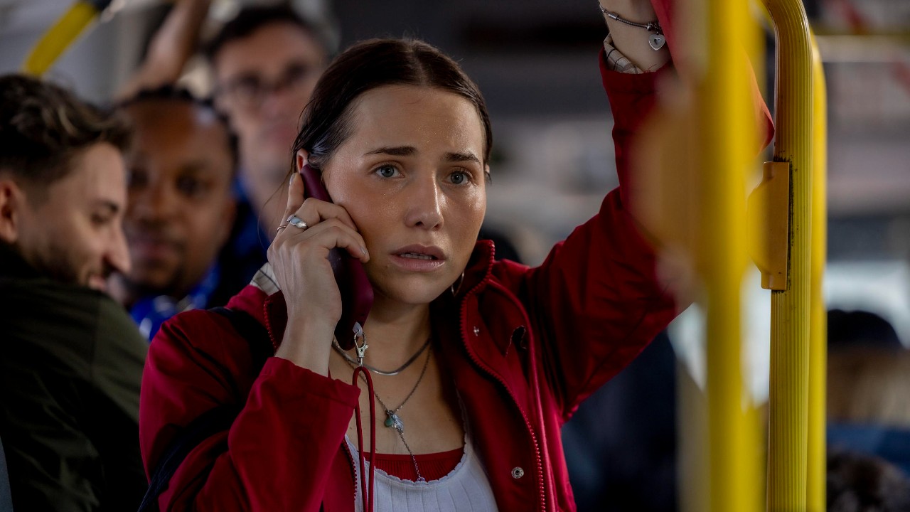 Adriana interpretada por Leticia Colin fala ao celular com expressão tensa dentro de ônibus lotado na novela Quem Ama Cuida