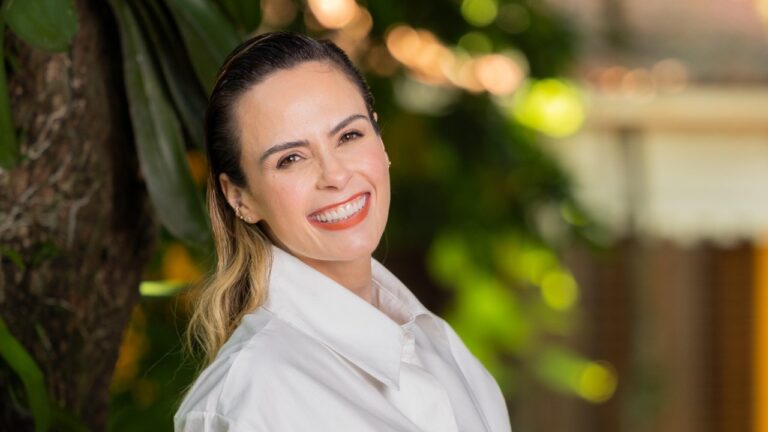 Ana Paula Renault sorri em retrato ao ar livre com fundo desfocado de plantas e iluminação quente