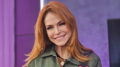 Babi Xavier sorri com cabelo ruivo solto e jaqueta verde em estúdio com fundo iluminado em tons de roxo