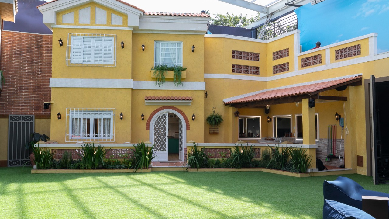 Fachada da Casa do Trampo no Casa do Patrão com paredes amarelas, jardim frontal e área externa coberta