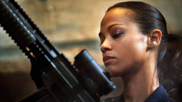 Cataleya interpretada por Zoe Saldaña segura rifle com mira e observa arma em cena do filme Colombiana: Em Busca de Vingança