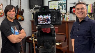 César Kiles e Ismar Madeira posam sorrindo em estúdio com câmera em primeiro plano, instrumentos musicais e piano ao fundo no Globo Repórter