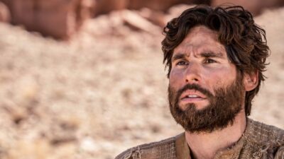 Jesus (Dudu Azevedo) com barba e túnica bege observa o horizonte em cenário árido da novela bíblica Jesus