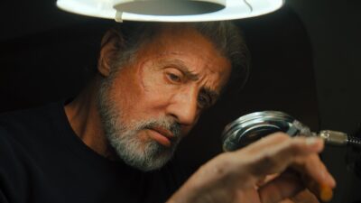 Sylvester Stallone como Joe examina objeto com lupa sob luz circular em cena do filme Samaritano com expressão concentrada