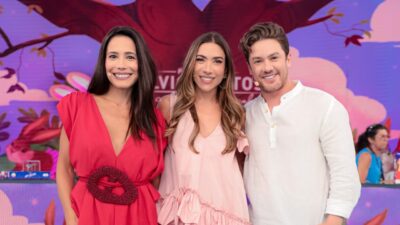 Ju Knust, Patricia Abravanel e Leonardo Miggiorin sorrindo no palco do Programa Silvio Santos com cenário colorido ao fundo