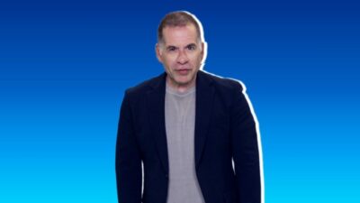 O ator Leandro Hassum encara a câmera com expressão neutra usando blazer azul marinho sobre camiseta cinza em fundo degradê azul e contorno branco