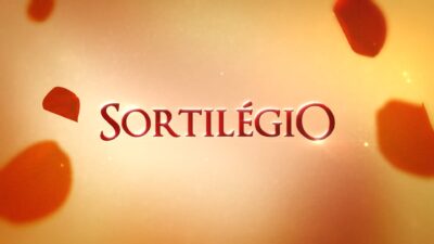 Logotipo da novela Sortilégio em letras vermelhas sobre fundo dourado com pétalas espalhadas ao redor