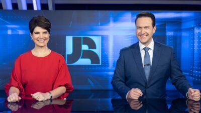 Mariana Godoy e Eduardo Ribeiro apresentam o Jornal da Record em bancada com logotipo do JR exibido ao fundo no estúdio