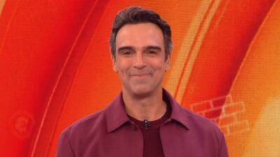 Tadeu Schmidt sorri no estúdio do BBB 26 com fundo em tons de laranja e iluminação de LED ao fundo