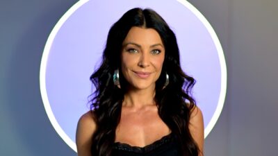 Ceci Ribeiro posa com vestido preto e brincos prateados diante de fundo lilás com círculo iluminado ao redor da cabeça