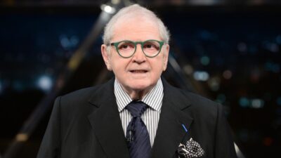 Jô Soares com óculos verdes e terno escuro durante apresentação em programa de televisão no estúdio
