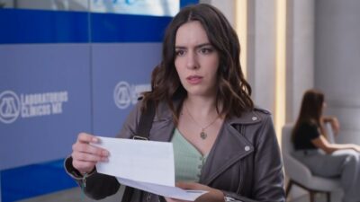 Joana (Camila Valero) segura documento com expressão preocupada em cena da novela A História de Joana, a Virgem