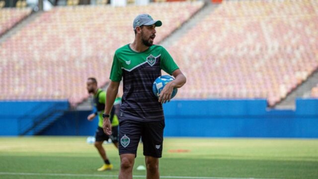 João Victor segura bola durante treino em campo de futebol com arquibancadas vazias ao fundo
